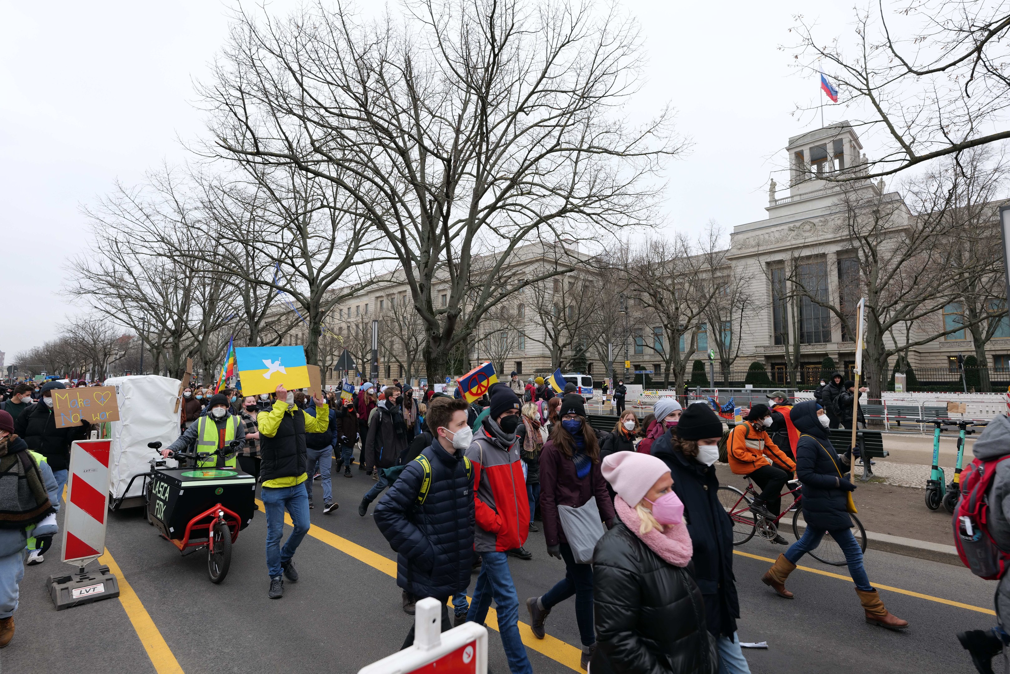 Eine große Gruppe von Menschen nimmt an einer Protestmarsch in Washington, D.C. am 21. Januar 2020 teil und geht eine Straße entlang, waß Plakate und Schilder haltend, einige fahren Fahrräder, mit Schilderständen, Bäumen und einem klaren blauen Himmel im Hintergrund.