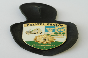 Ein Polizeistern mit der Aufschrift "Polizei Berlin" darauf, mit einem blauen Hintergrund und einem weißen Stern in der Mitte, umgeben von einem weißen Rand.