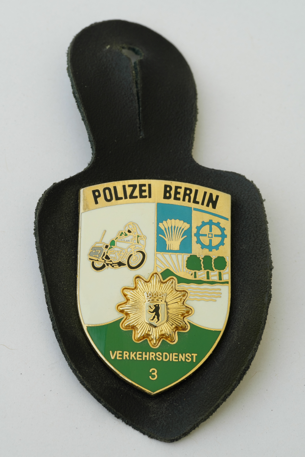 Ein Polizeistern mit der Aufschrift "Polizei Berlin" darauf, mit einem blauen Hintergrund und einem weißen Stern in der Mitte, umgeben von einem weißen Rand.
