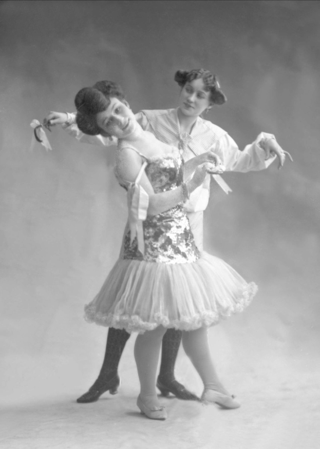 Zwei Frauen in einem Schwarz-Weiß-Foto tanzen synchron, eine hält ein Band, tragen passende Kleider.