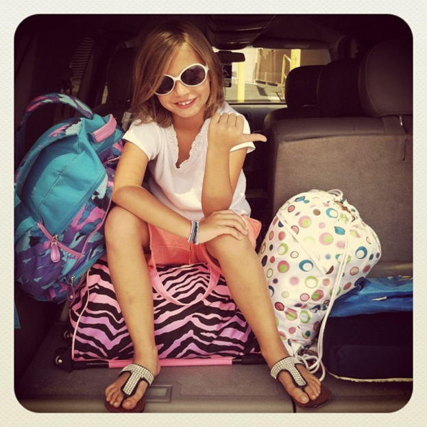 Ein Mädchen mit Brille sitzt auf einem Koffer mit einem Koffer in der Nähe.