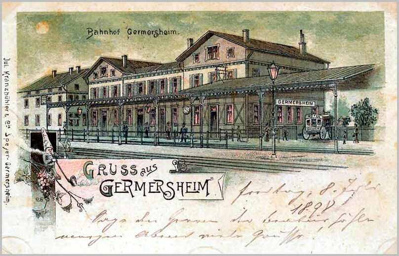 Schwarz-weiß-Postkarte des Bahnhofs Germersheim in Deutschland, die ein Gebäude mit Fenstern, einen Zaun, einen Straßenpfahl, Menschen, Fahrzeuge, Bäume und einen bewölkten Himmel zeigt.