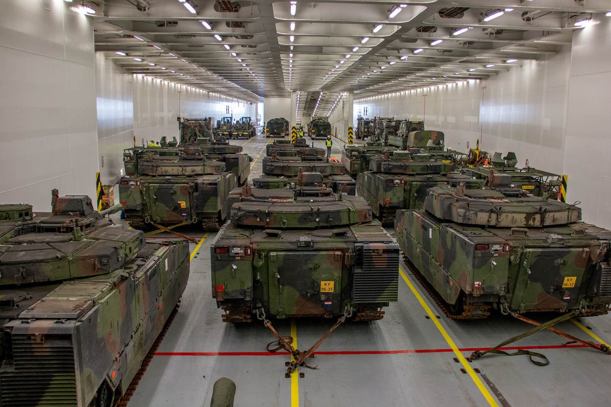 Eine gro├če Militargrundstückhalle mit Reihen von Militartanks, W├Ąnden an beiden Seiten und Deckenleuchten.