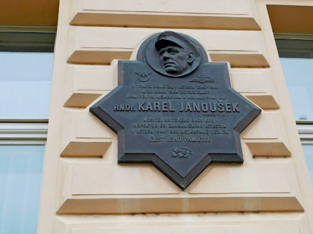 Plaque featuring an image of a man in a hat, mounted on a building with glass windows, inscribed with "Karel Janousek, the founder of the Soviet Union".