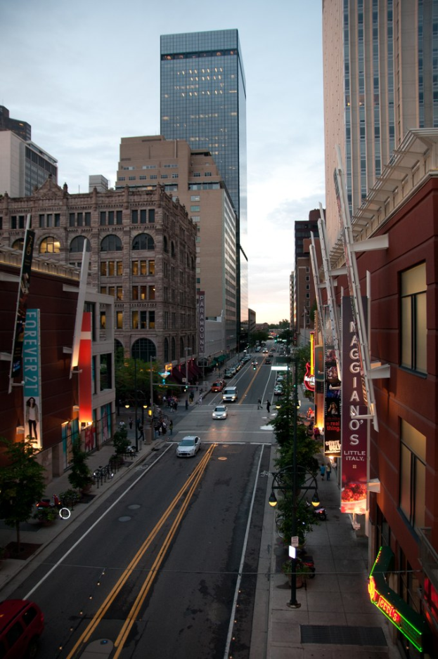 Stadtsicht mit Stra├če, fahrenden Autos und hohen Geb├Ąuden auf beiden Seiten unter einem klaren Himmel.
