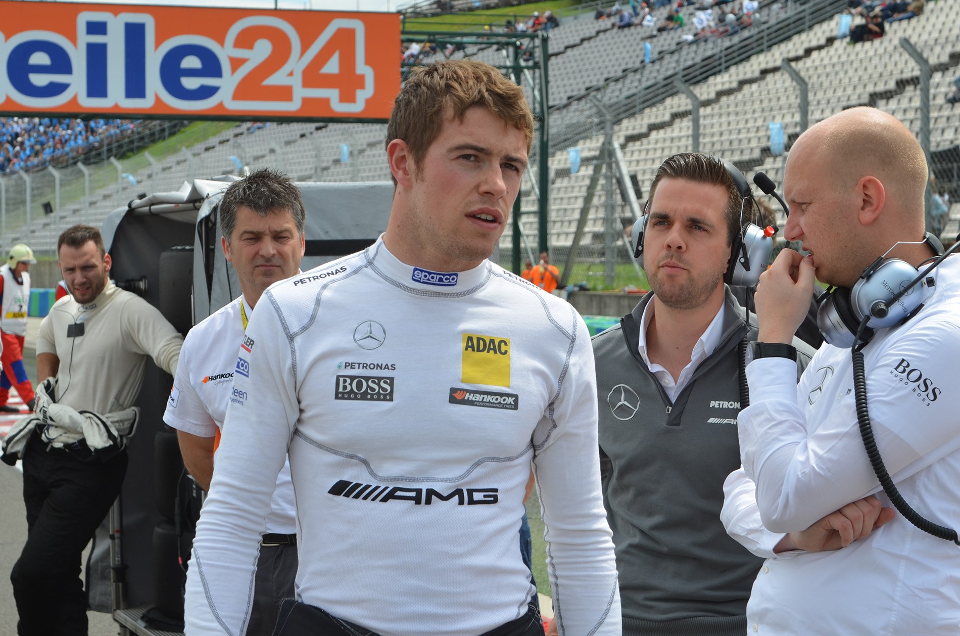 Nico Rosberg, Mercedes AMG Petronas F1 Team Principal, steht in der Mitte umgeben von Menschen mit Headsets, mit Zuschauern auf den Rängen, einem Werbeplakat und einem klaren blauen Himmel im Hintergrund.