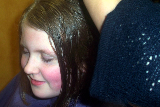 Ein Mädchen mit einem Lächeln und geschlossenen Augen steht vor einer Wand.