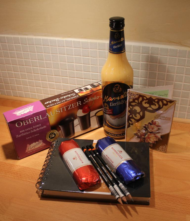 Ein Tisch mit einem Tagebuch, Stiften, Keksen, einem Getränk und einer Grußkarte vor einer Wand.