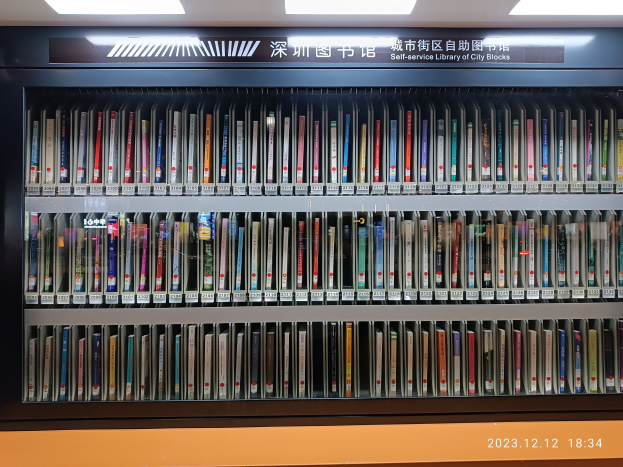 Eine gut beleuchtete Bibliothek mit hohen Bücherregalen voller Bücher, eine sichtbare Tafel mit Text und ein Wasserzeichen unten, das einer Selbstbedienungsbibliothek in Stadtblocks ähnelt.