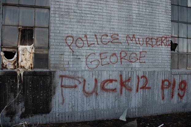 Ein Gebäude mit der Graffiti-Aufschrift "Polizeimord George Fuck 12 P19" an der Seite, mit Fenstern und diversen Gegenständen davor