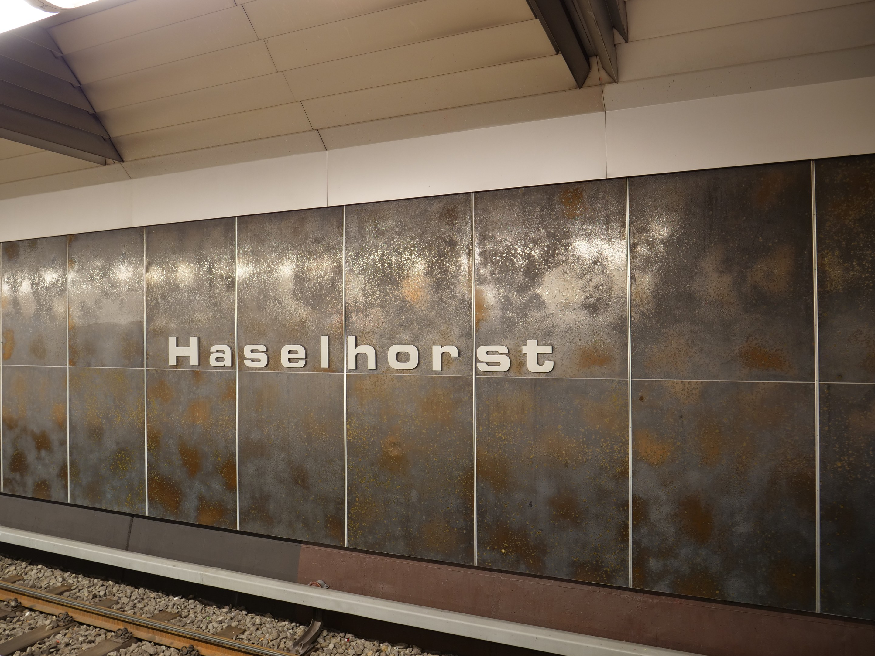 A train station platform with a "Haselhorst" sign illuminated by overhead lights in Berlin, Germany.