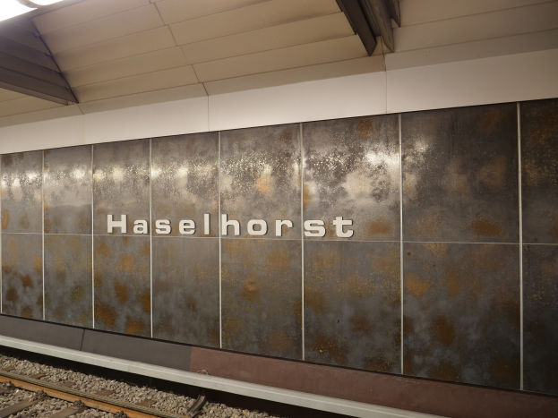 A train station platform with a "Haselhorst" sign illuminated by overhead lights in Berlin, Germany.