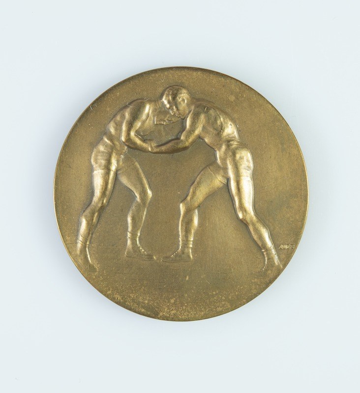 Goldmedaille mit zwei ringenden Männern auf weißem Hintergrund.