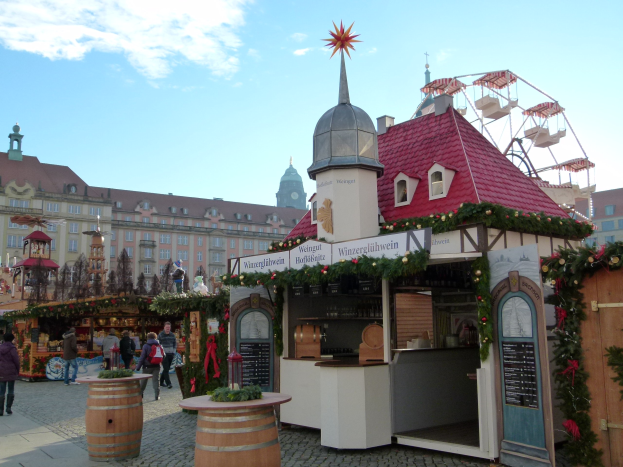 Ein belebter Weihnachtsmarkt in Nürnberg, Deutschland mit Menschen um geschmückte Stände, festliche Lichter, Schmuck, Gebäude im Hintergrund, einem Riesenrad und einer Tafel mit Text auf der rechten Seite.
