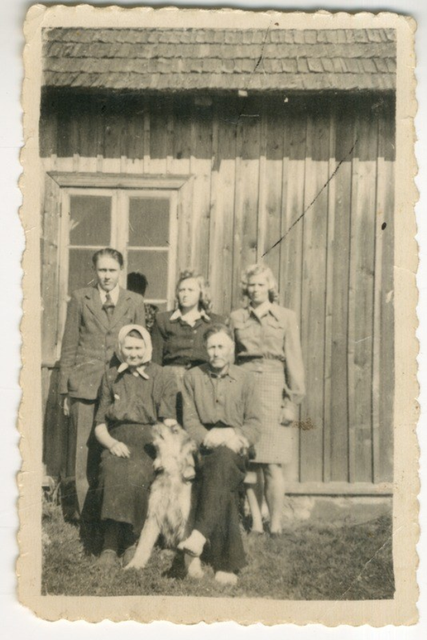 Schwarz-weiß-Foto einer Familie mit einem Hund vor einem Haus mit einem Fenster.