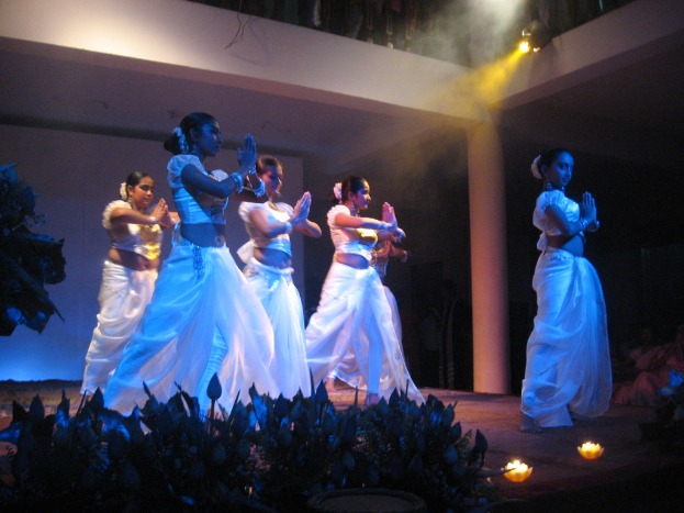 Eine Gruppe von Menschen tanzt auf einer Bühne mit einer Gruppe von Pflanzen davor, während eine andere Gruppe zuschaut.