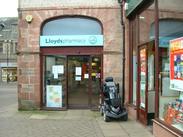 Eine Apotheke mit einem vor dem Eingang geparkten Auto und einem Gebäude auf der linken Seite.