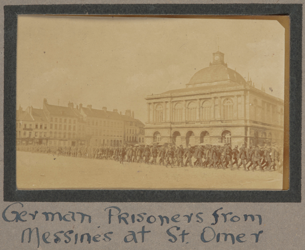 Eine Gruppe deutscher Kriegsgefangener aus Messines steht vor einem Gebäude an einem klaren blauen Himmel, mit Text am unteren Bildrand.