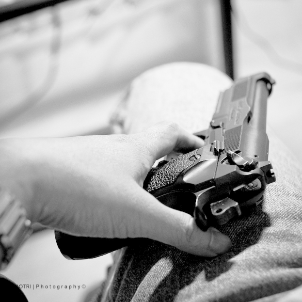 Ein unscharfer Schwarz-Weiß-Bild einer Hand, die eine Waffe hält und auf dem Bein ruht, mit einem Wasserzeichen in der rechten unteren Ecke.