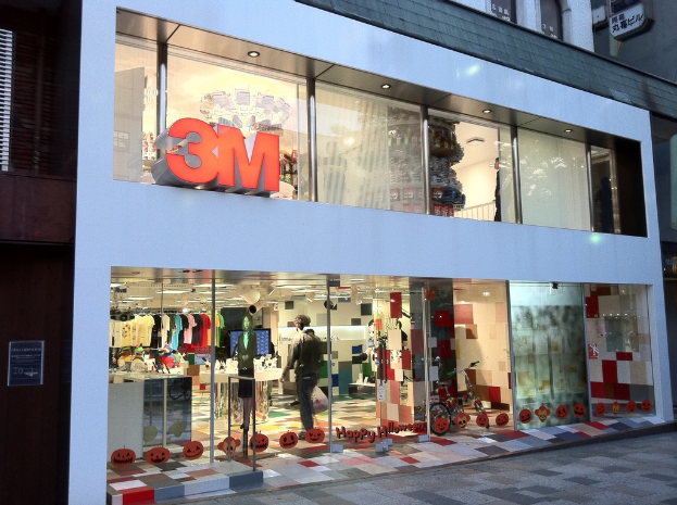 Ein Gebäude mit einer Glaswand, die Kleider auf Bügeln, eine Schaufensterpuppe, ein Fahrrad, geklebte Bilder und Schrift auf der Glaswand zeigt.