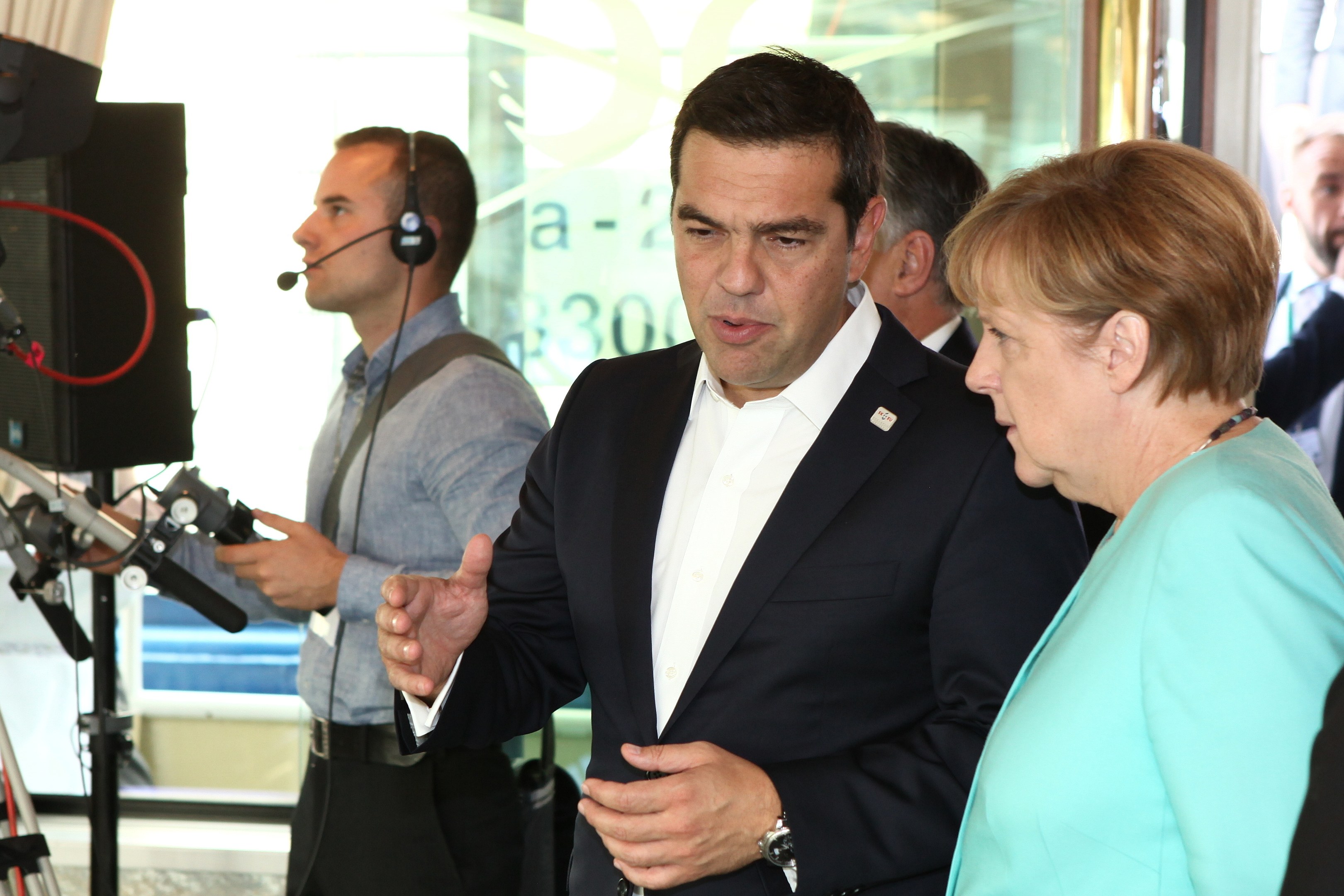 Bundeskanzlerin Angela Merkel und ehemaliger Bundeskanzler Joachim Gauck sprechen vor einer Glaswand mit einem Vorhang im Hintergrund, beide tragen Anzüge und Mikrofone.