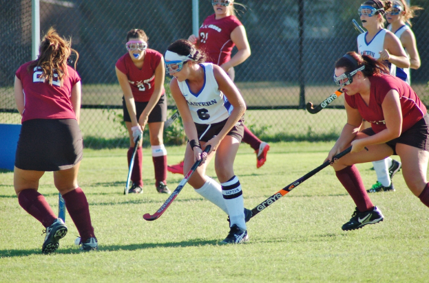 Frauen beim Hockey auf einem Rasenfeld mit einem Maschendraht-Hintergrund.
