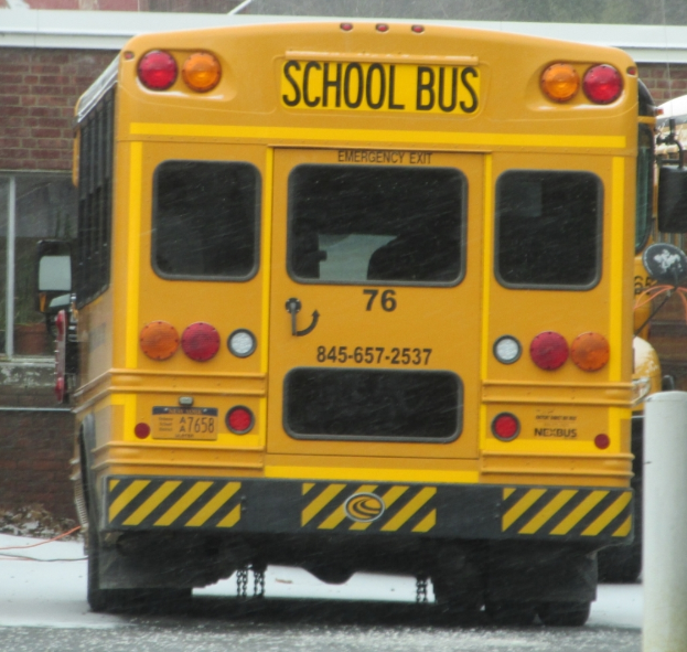 Ein gelber Schulbus parkt vor einem Backsteinbau mit Fenstern.