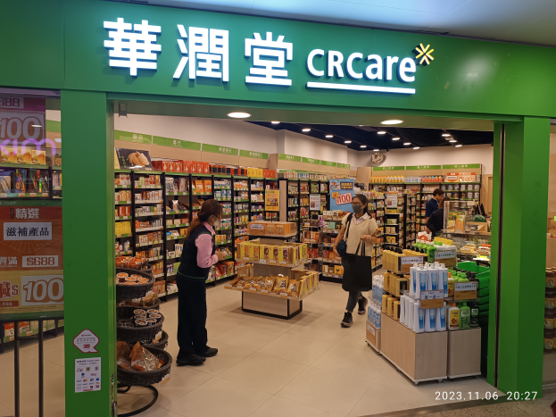 Eine Gruppe von Menschen steht vor einem Geschäft mit einer Tafel, auf der 'crcare' steht, mit Regalen voller Lebensmittel, Flaschen und anderen Gegenständen im Inneren und einer Tafel mit Text auf der linken Seite.