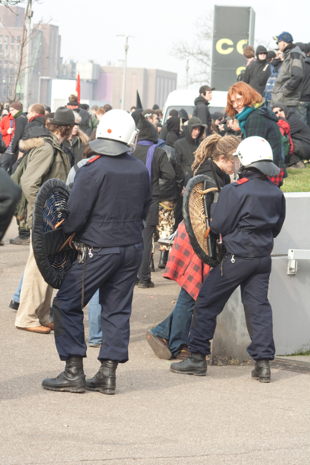 Eine Gruppe von Menschen, die auf einer Straße mit zwei Personen in der Mitte gehen, die wie Polizisten aussehen, Gebäude im Hintergrund und Boden unten.