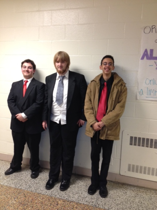 Drei M√§nner in Sakkos, Krawatten und Schuhen, die auf einem Boden mit einer Wand und einem Plakat im Hintergrund stehen.