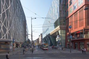 A busy city street with tall buildings, street infrastructure, vehicles, pedestrians, and a clear blue sky.