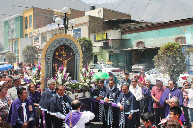 Menschen auf einer Straße mit einem Kreuz und Blumensträußen in der Mitte, Autos im Hintergrund und Gebäude, Bäume und Straßenlaternen im Hintergrund.