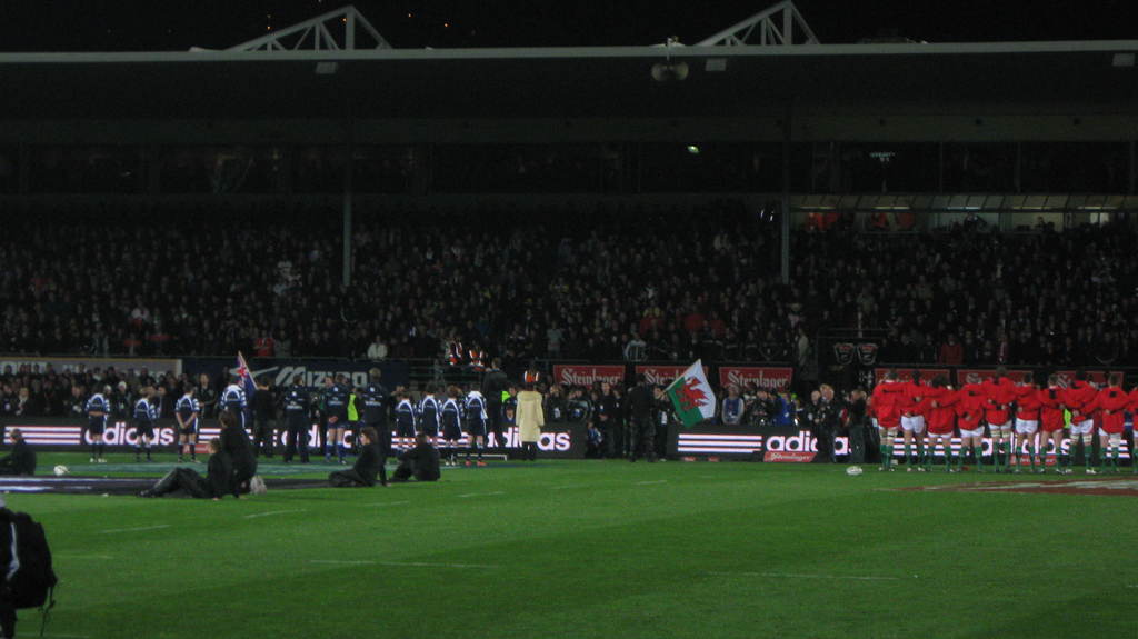 Eisernes Gitter und Lautsprecher oben auf dem Bild, mit einer Menge, Werbung, Flagge und Boden unten.
