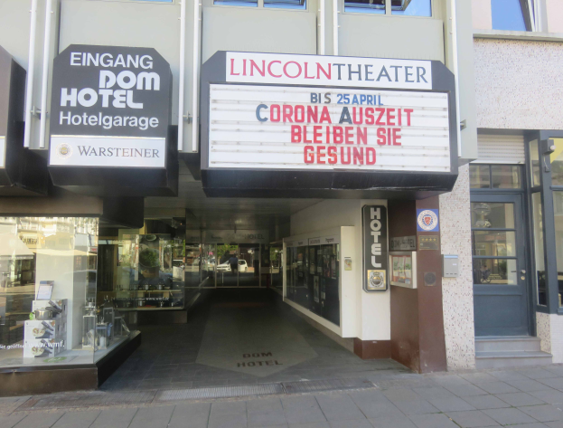 Das Lincoln Theater in Berlin, Deutschland, ein Gebäude mit Glasfenstern und -türen sowie einer Tafel mit Text darauf, das verschiedene Objekte im Inneren zeigt und so den Eindruck einer pulsierenden Stadtlandschaft vermittelt.