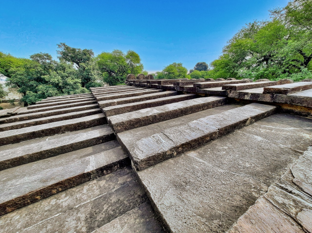 Stone steps leading to the top of the Chhatrapati Shivaji Maharaj Temple, a UNESCO World Heritage Site in India, with green trees and a blue sky in the background.