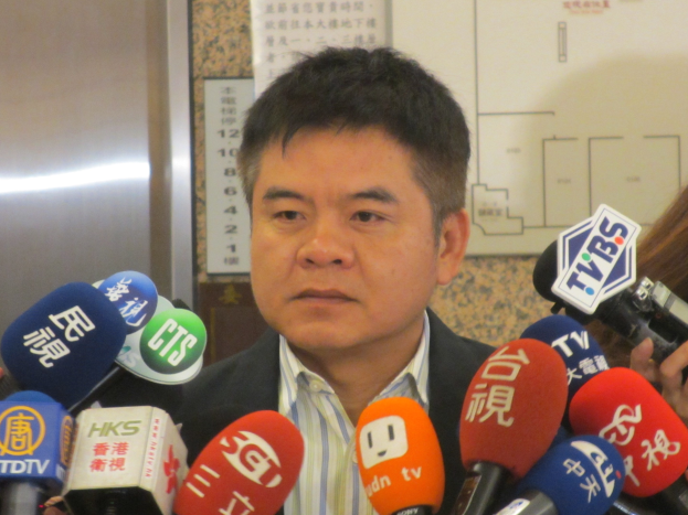 Ein Mann im Anzug spricht mit Reportern, während eine Frau mit einer Kamera rechts von ihm steht.