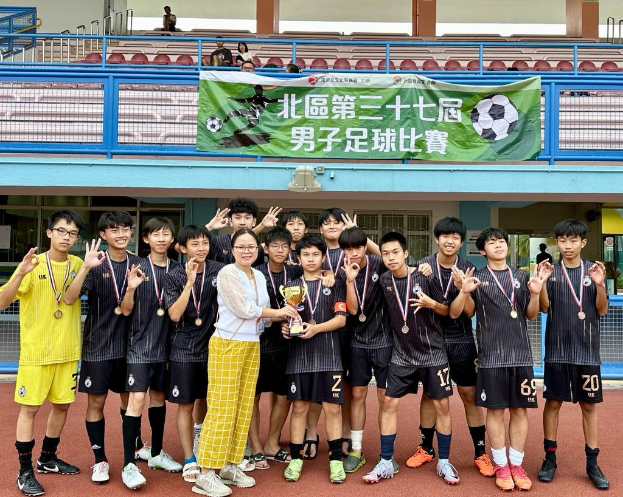 Group of young men in soccer uniforms standing on a field holding a trophy and wearing medals, with a banner labeled "Yokohama U-16 Boys Soccer Team" in the background.