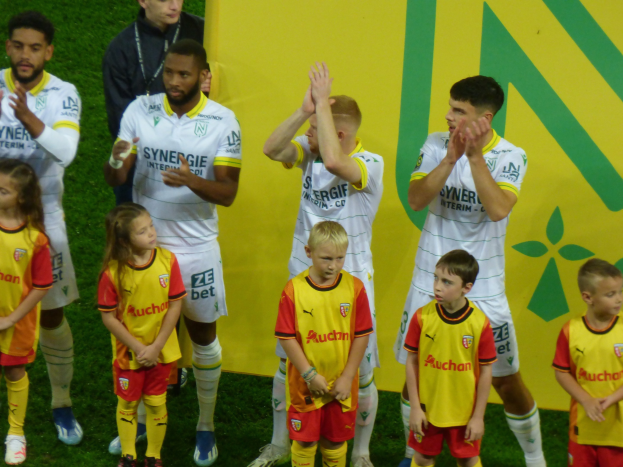 A group of soccer players in uniforms clapping on a field with a "Ligue 1" sign in the background, celebrating a victory.