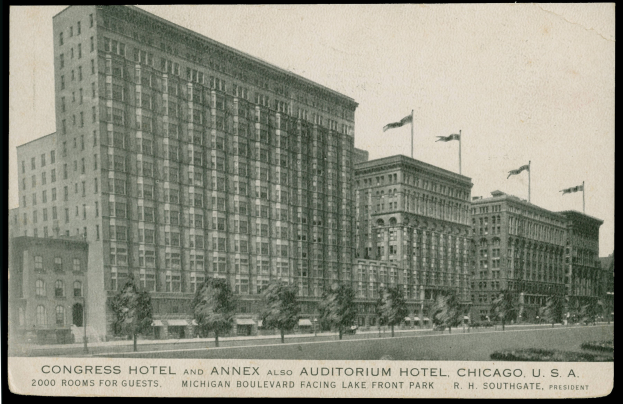 Ein Schwarz-Weiß-Foto des Congress Hotels und des Annex Auditorium Hotels in Chicago, Illinois, ein großes Gebäude mit vielen Fenstern, umgeben von Bäumen und Fahnenstangen, mit einem klaren Himmel im Hintergrund und Text am unteren Bildrand.