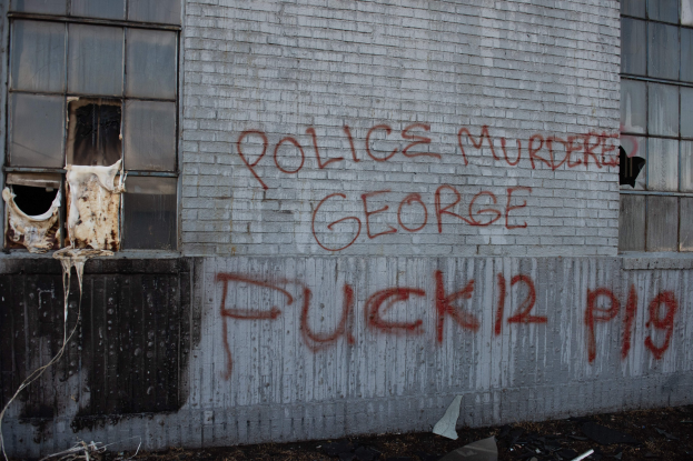 Graffiti auf einem Gebäude mit der Aufschrift "Polizei ermordet George Fuck 12 P19" mit Fenstern und verstreuten Gegenständen davor.