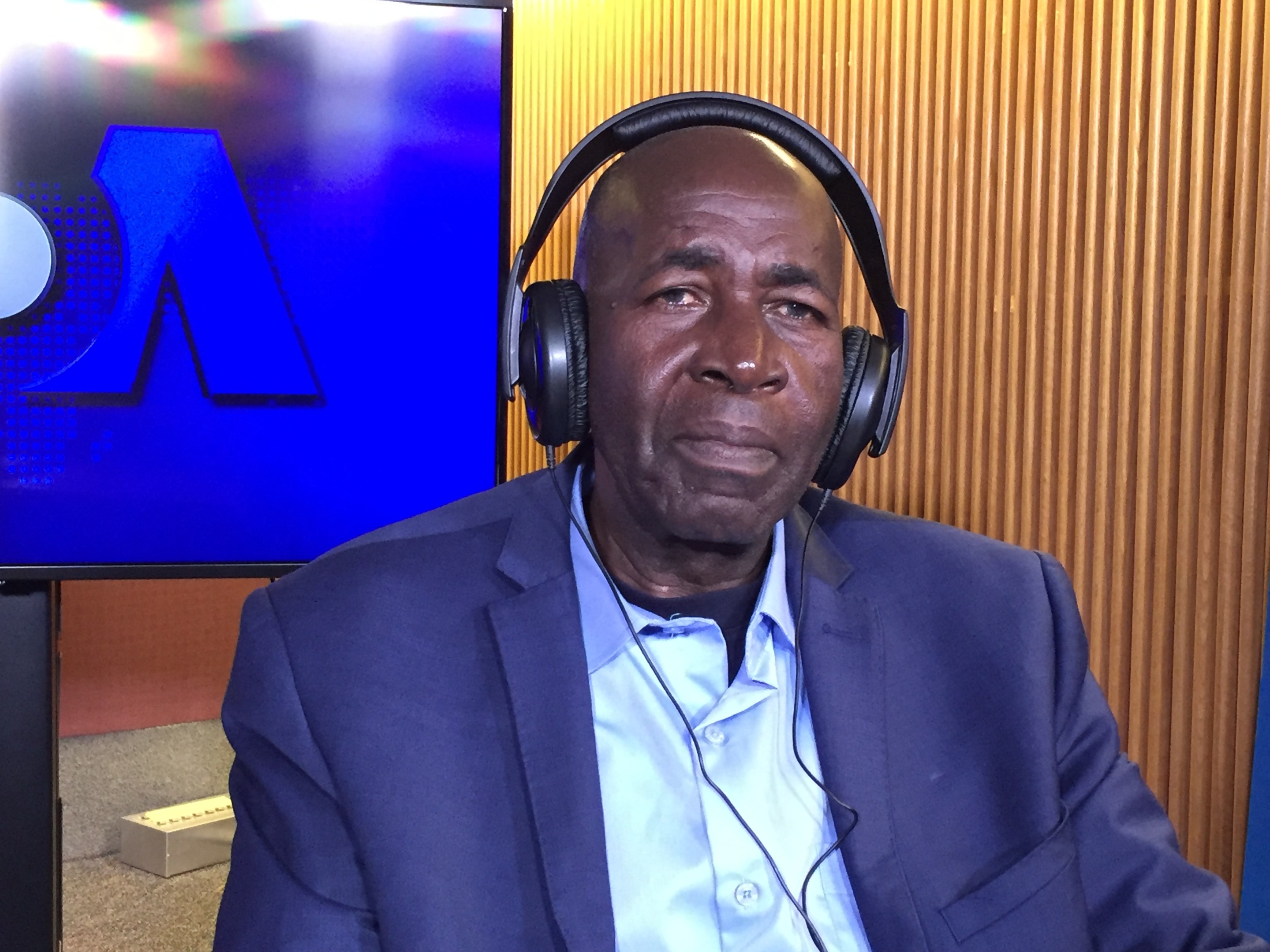 Ein Mann im Anzug mit Kopfhörern sitzt vor einem Fernseher mit einer hölzernen Wand dahinter und scheint über das Internetverbot der nigerianischen Regierung zu sprechen.