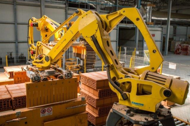Großes industrielles Lager mit gestapelten Kisten, Kränen, Zaun, Pfosten und einer fernen Wand in einer automatisierten Fertigungsumgebung.