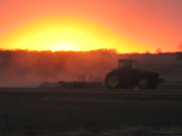 Ein Traktor auf einem Feld mit Bäumen und Himmel im Hintergrund.
