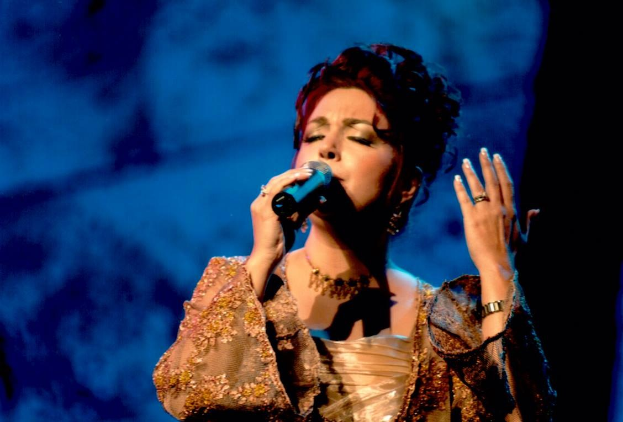 Eine Frau in einem goldenen Kleid, die auf der Bühne in ein Mikrofon singt, mit einem blauen und schwarzen Hintergrund, bei der Eurovision Song Contest.