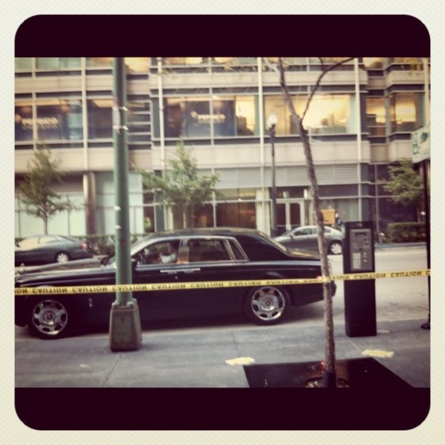 Ein Auto ist in der Mitte des Bildes zu sehen, umgeben von Pfählen und Bäumen, mit einem Gebäude, Fahrzeugen, Bäumen, Pflanzen und Lichtern im Hintergrund und einem Weg am unteren Rand.