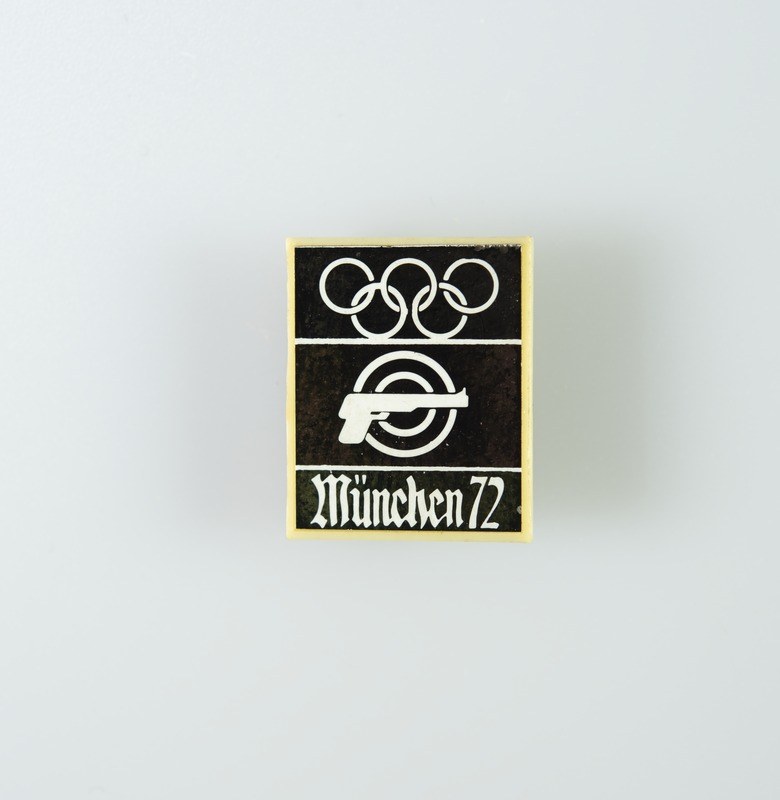 Black and white logo for the 1972 Munich Olympics featuring a stylized figure with outstretched arms inside a circle and the text "München 1972" in bold black font.