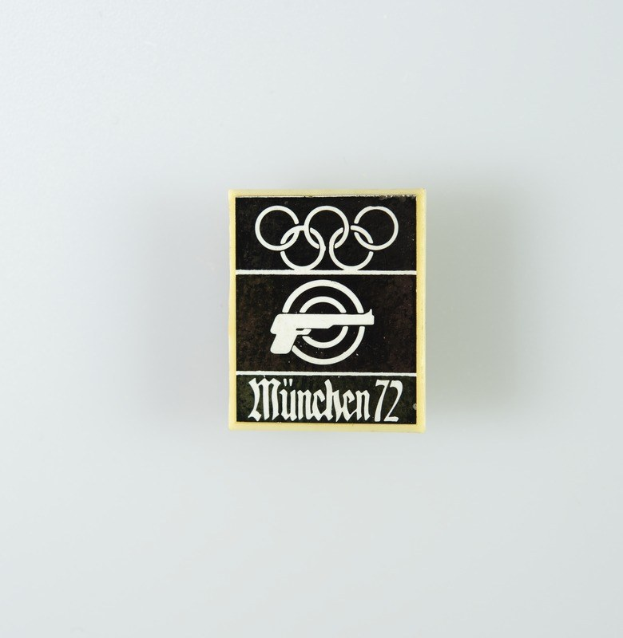 Black and white logo for the 1972 Munich Olympics featuring a stylized figure with outstretched arms inside a circle and the text "München 1972" in bold black font.