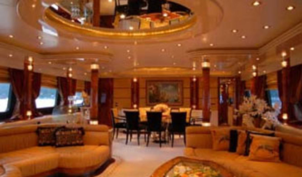 Ein Hotel-Foyer mit Sofas, Stühlen, Tischen und Blumenarrangements im Vordergrund, Fenstern mit Vorhängen und Lampen auf beiden Seiten, einem gerahmten Kunstwerk und Deckenleuchten im Hintergrund und einem großen Spiegel oben.