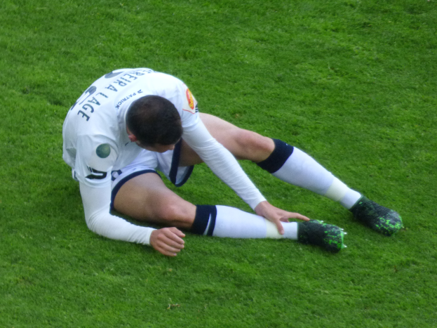Ein Fussballspieler sitzt auf dem Boden und hat den Kopf in den Händen, trägt eine Sportuniform und Fußballschuhe.