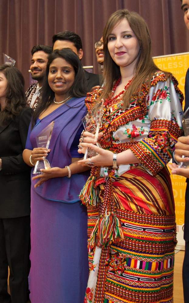 Eine Gruppe von Menschen auf einer Bühne mit einer Frau in der Mitte, die einen Pokal hält, hinter einem Vorhang mit einer Tafel, auf der "Bravo Segen Award Gewinner" steht.